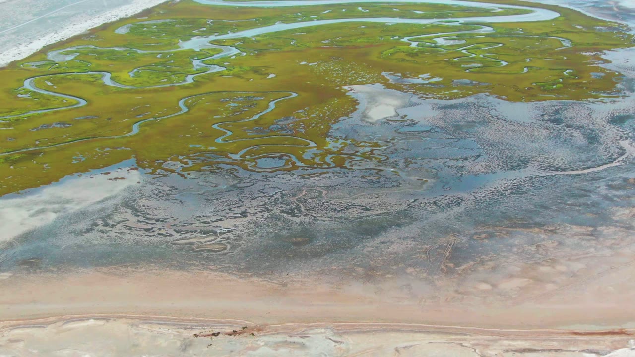 Overhead view at Punta Abreojos showing green marsh channels above shallow tidal water and pale sand flats, with no visible people.