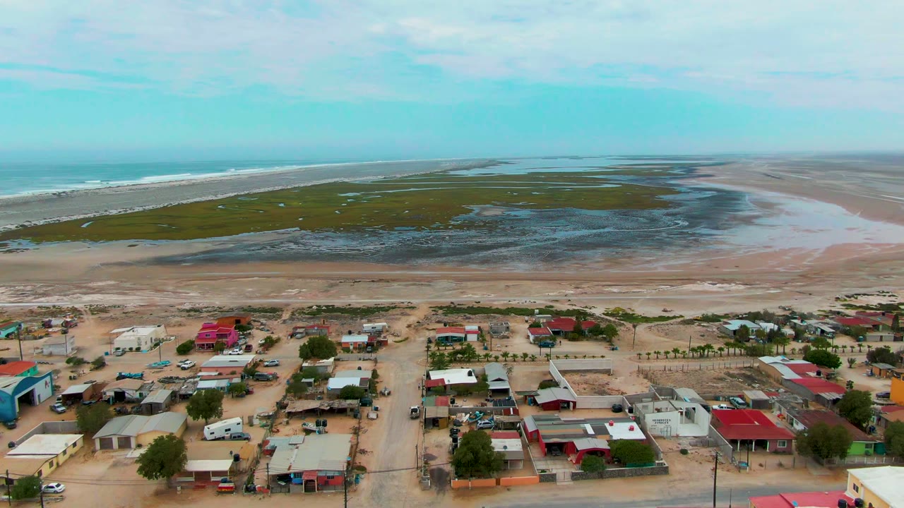Coastal settlement with sandy roads, marsh flats, and ocean beyond