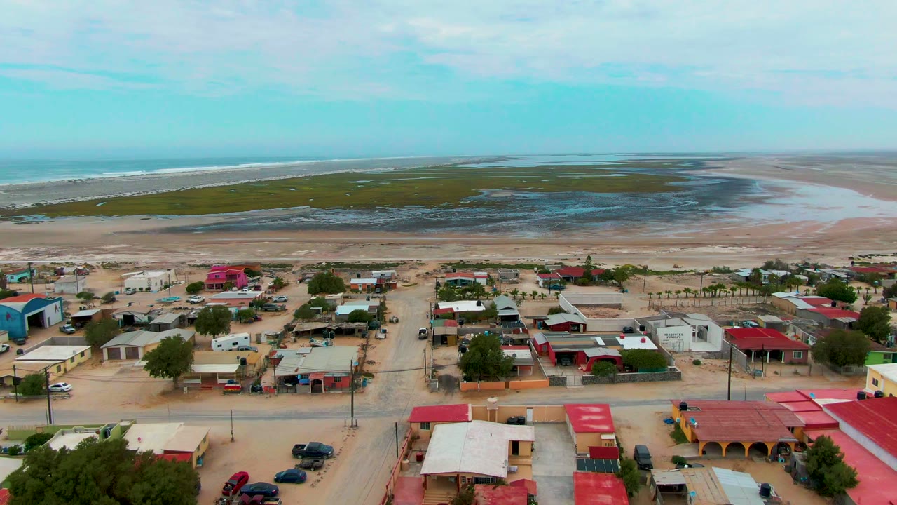 Drone view across beachside homes toward tidal flats and the ocean.