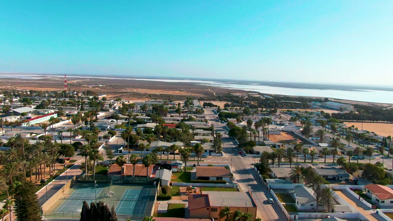 Residential blocks with palm trees, tennis courts, a tower, and water on the horizon.