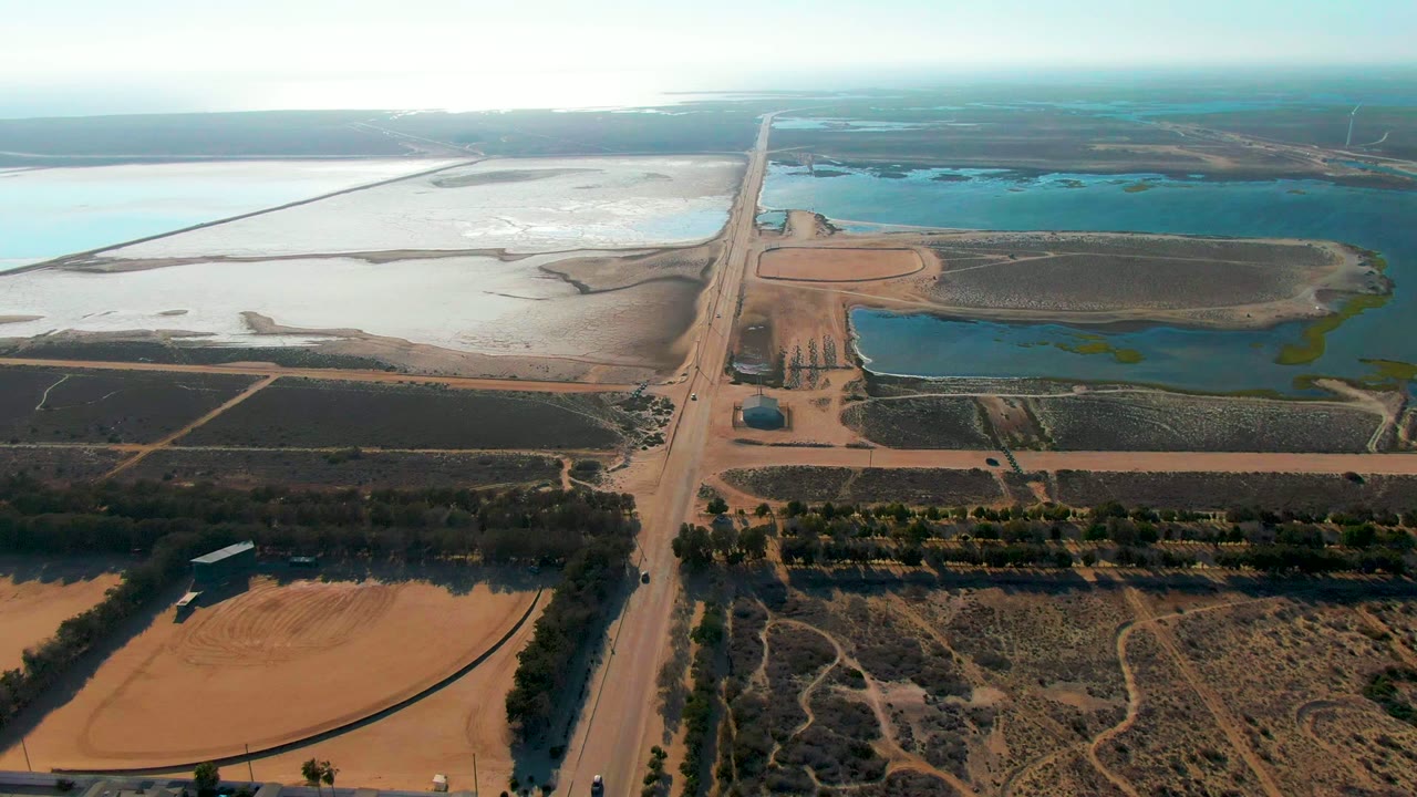 Dirt road crossing farmland beside blue and pale water areas.