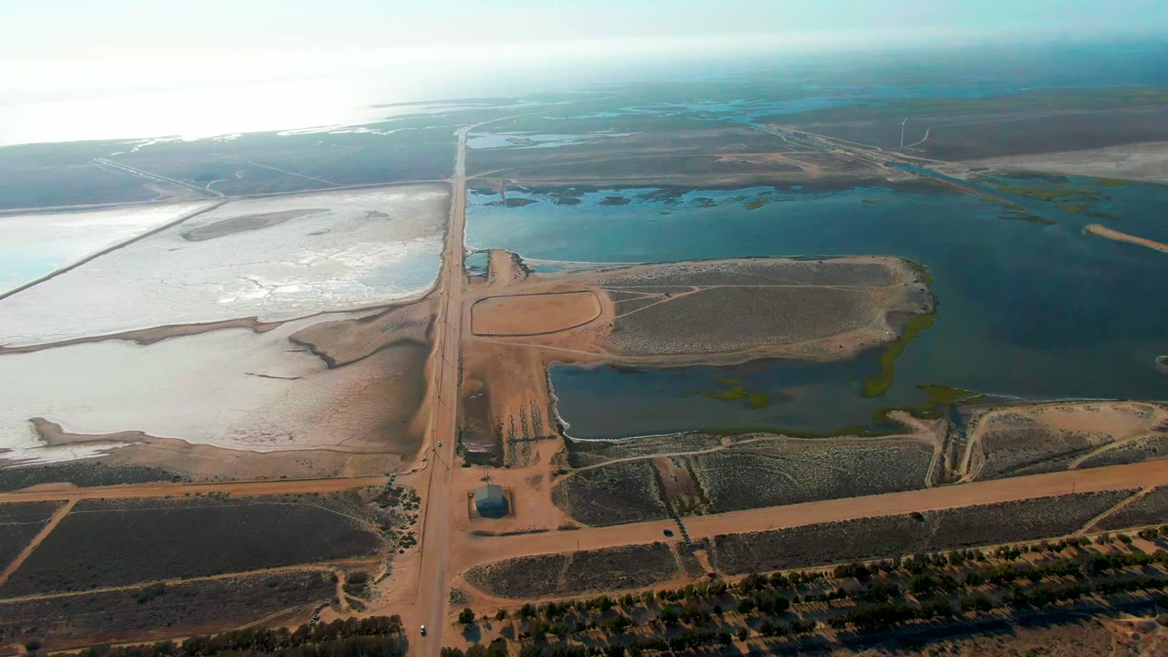 Drone view of a straight dirt road crossing fields and water ponds.