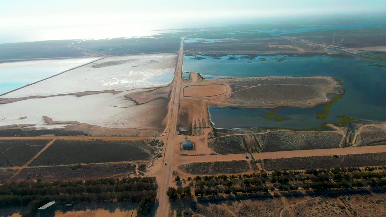 Drone view of a central dirt road beside blue-green water ponds