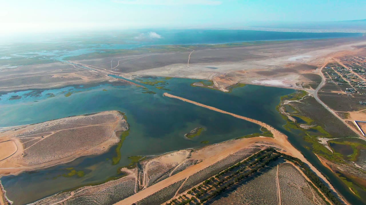 Wide drone view of a water basin with roads, dry terrain, and settlement edge.