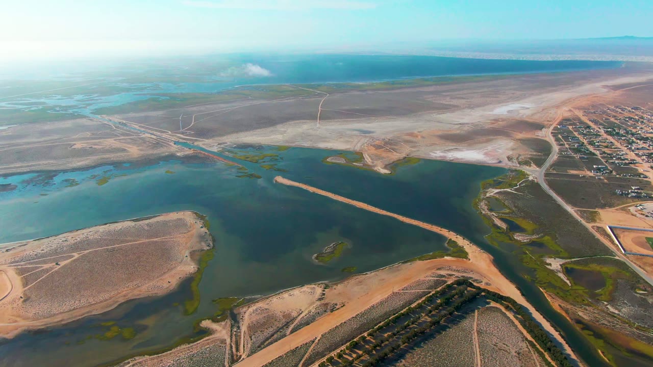 High aerial over reservoir water, sand bars, roads, and pale salt-flat-like land.