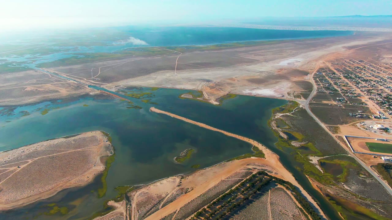 Drone view across lagoon water, sandbars, roads, and settlement edge