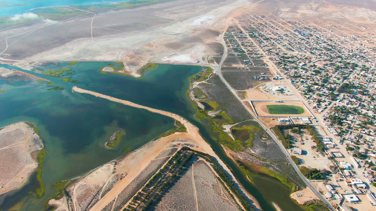 Aerial view in Guerrero Negro, Baja California Sur showing blue-green water, sandy banks, a road, and a dense residential grid with no visible people.