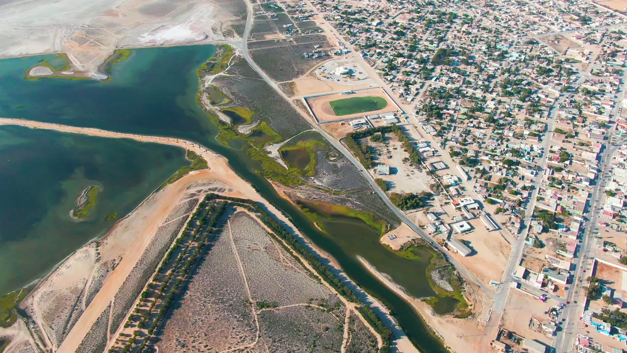 Drone view of coastal water, sandbar, channels, roads, and neighborhood blocks.