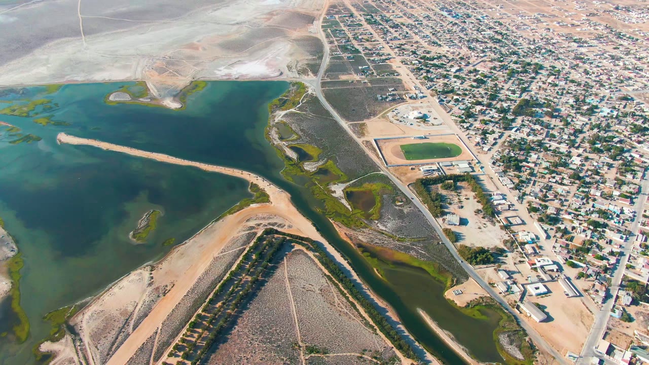 High aerial view of a town beside a broad water body and sandy channel.