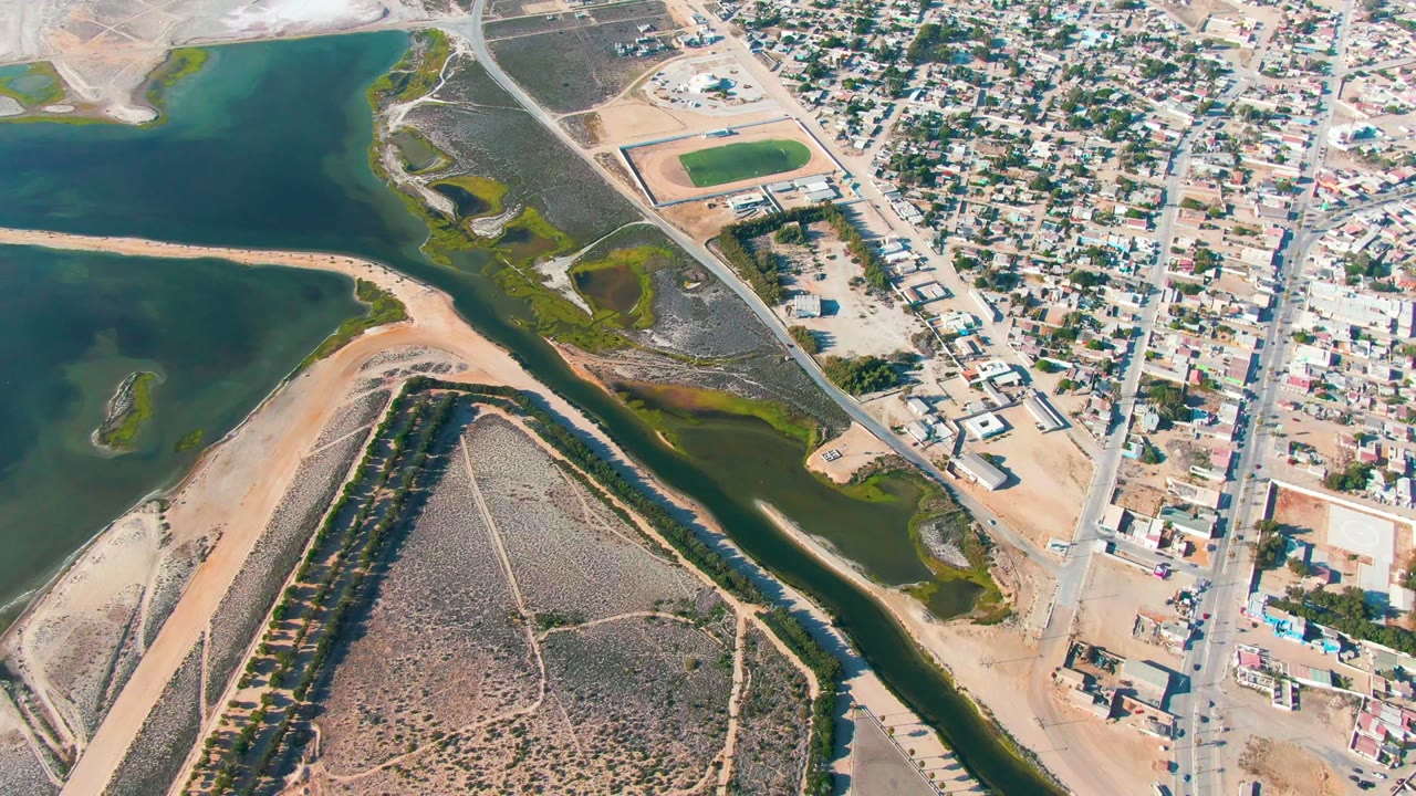 Aerial town edge with water channels, roads, and sandy terrain.