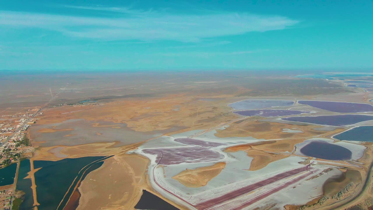 Drone view of salt ponds with a road and buildings along the left side.