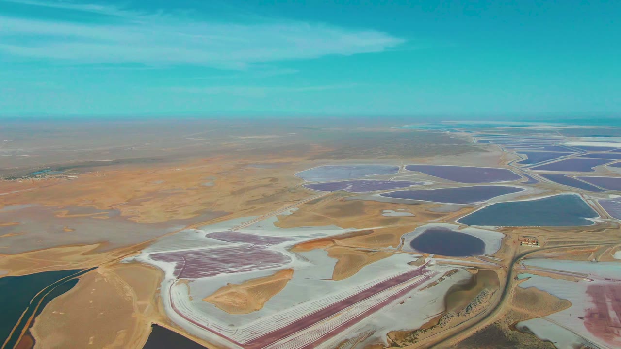 Drone view across colorful evaporation ponds and flat arid land.
