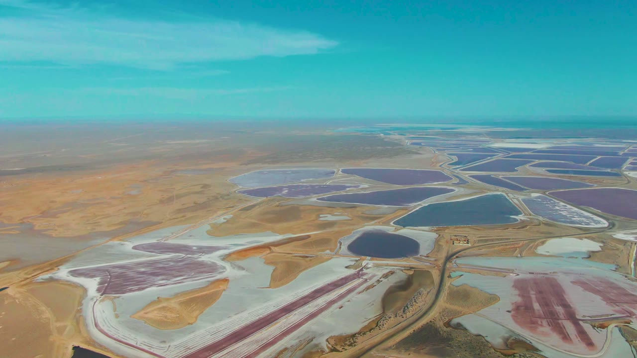 Drone view across patterned salt ponds and white flats in a dry landscape.