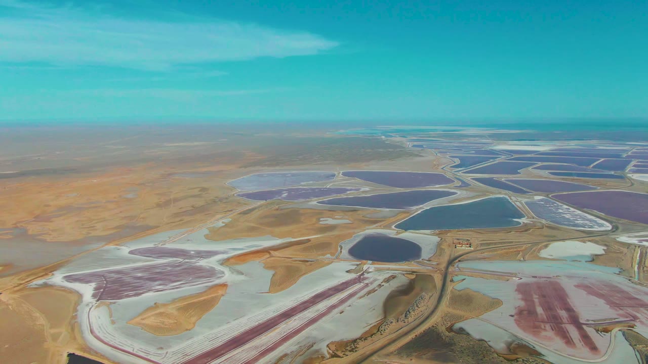 Wide drone view of Guerrero Negro salt evaporation ponds, showing pink ponds at lower right, white salt beds at lower left, blue basins in the middle, and no visible people.