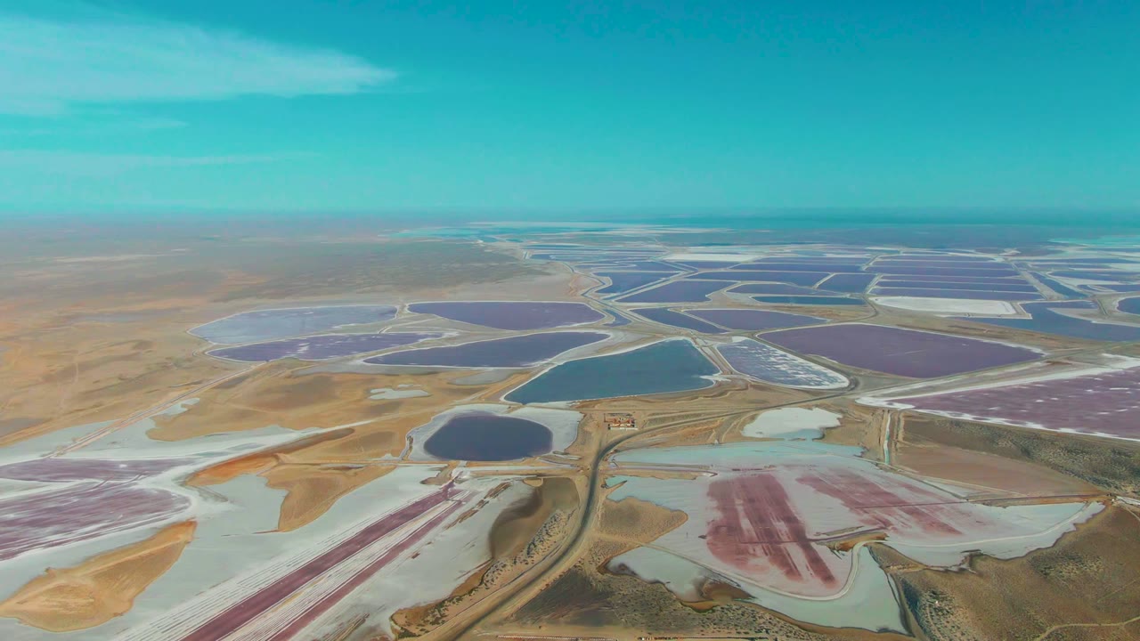 High aerial view of colored evaporation basins and pale salt flats.