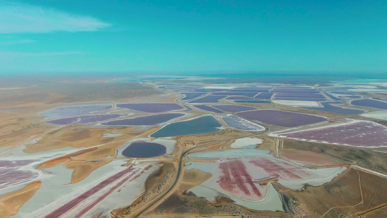 Wide aerial of pink and blue evaporation ponds crossed by dirt berms.