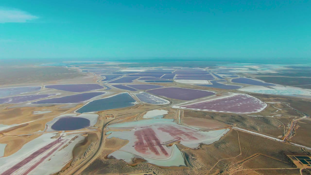 Aerial view over Guerrero Negro salt evaporation ponds with pink, purple, blue, and pale water basins separated by roads and berms, with no visible people.