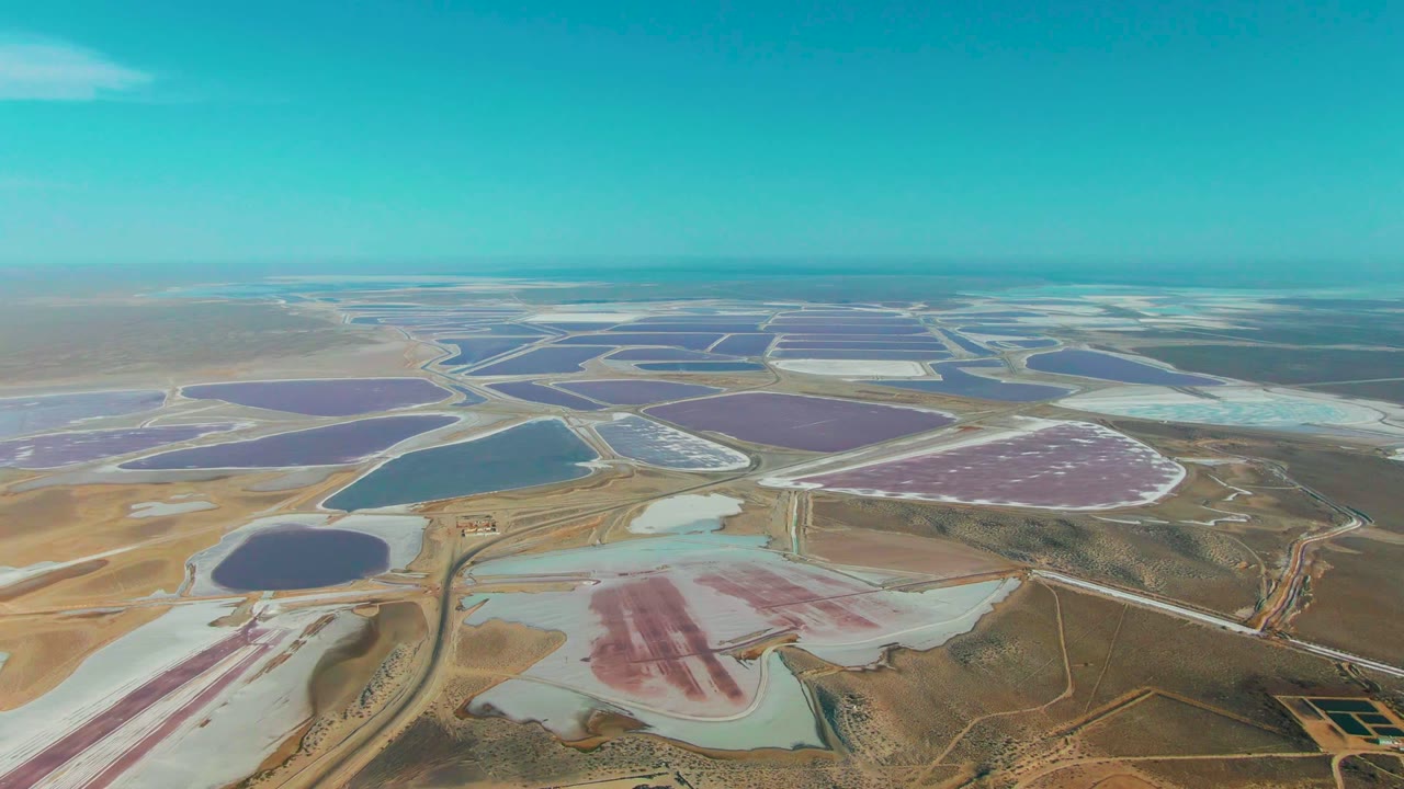 Wide aerial view of salt ponds divided by roads and dry earth.