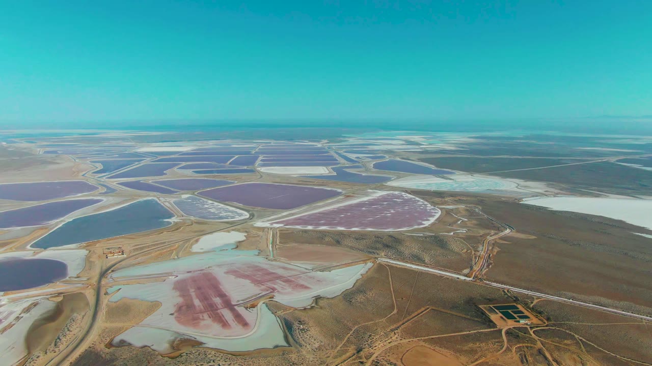 Aerial view over Guerrero Negro salt evaporation ponds with blue, purple, pink, and pale basins divided by dirt berms, with no visible people.