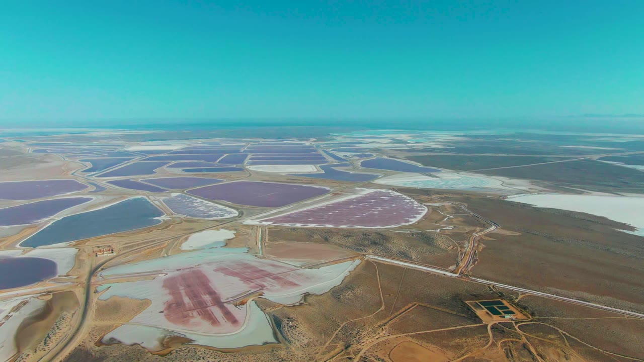 Wide drone view of salt ponds and service roads across arid land