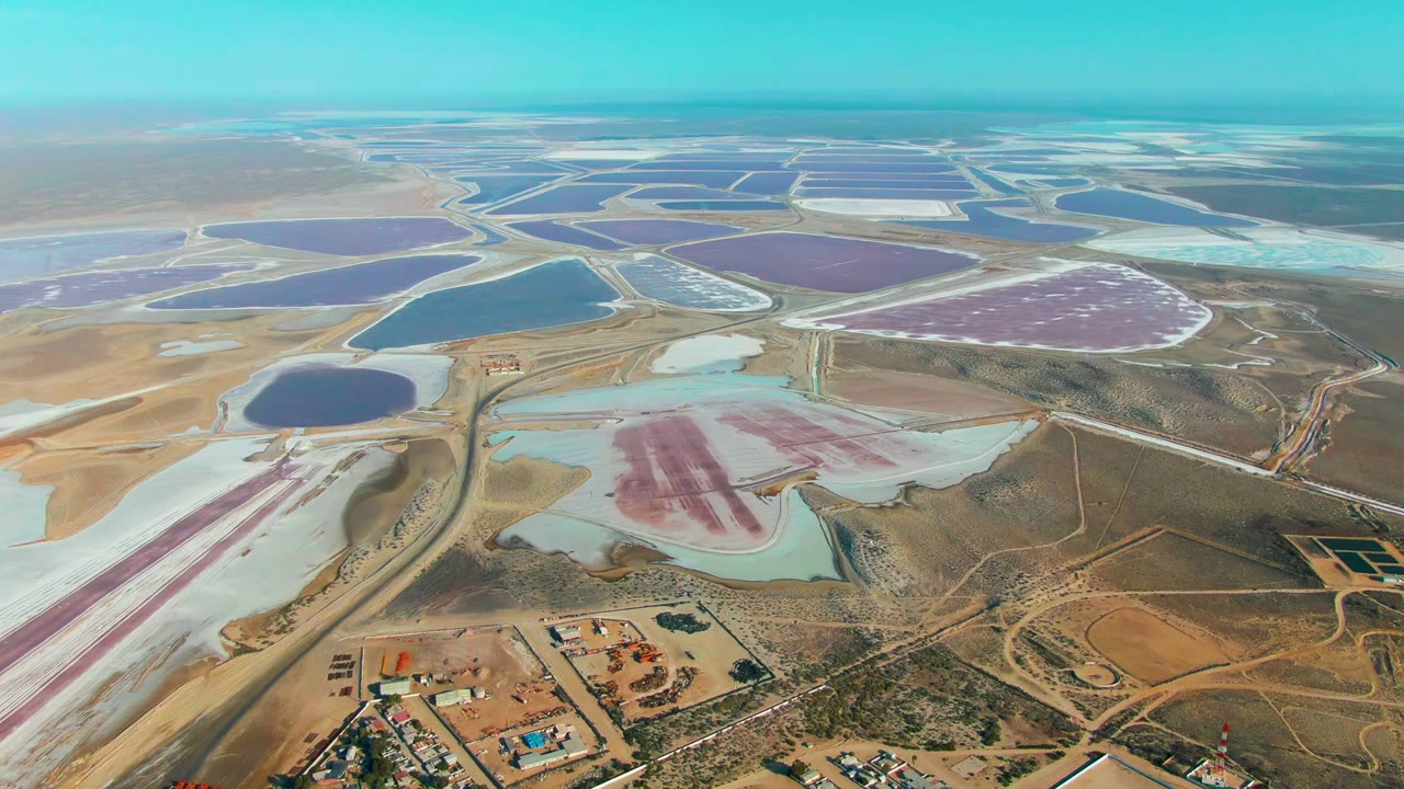Opening aerial frame over Guerrero Negro, Baja California Sur salt evaporation ponds, with pink, purple, blue, teal, and white basins divided by roads and no visible people.