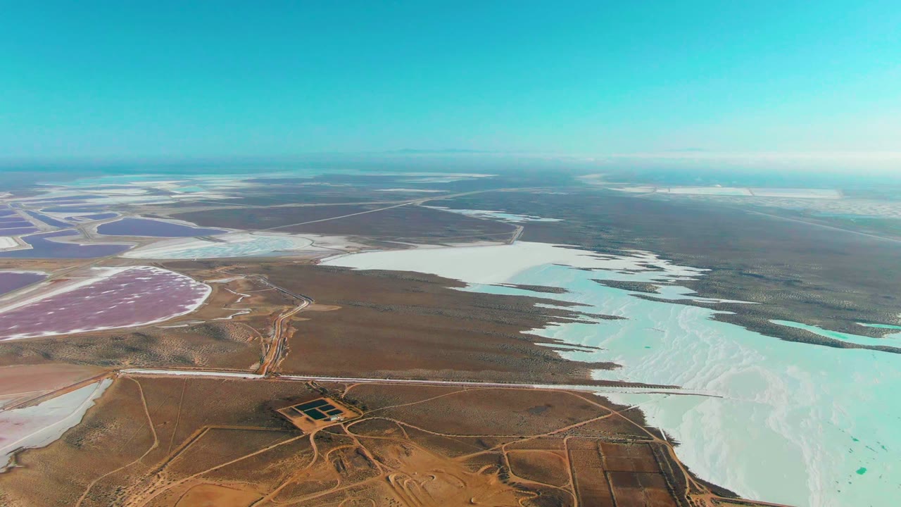 High aerial over white and turquoise evaporation ponds with roads and dry land.