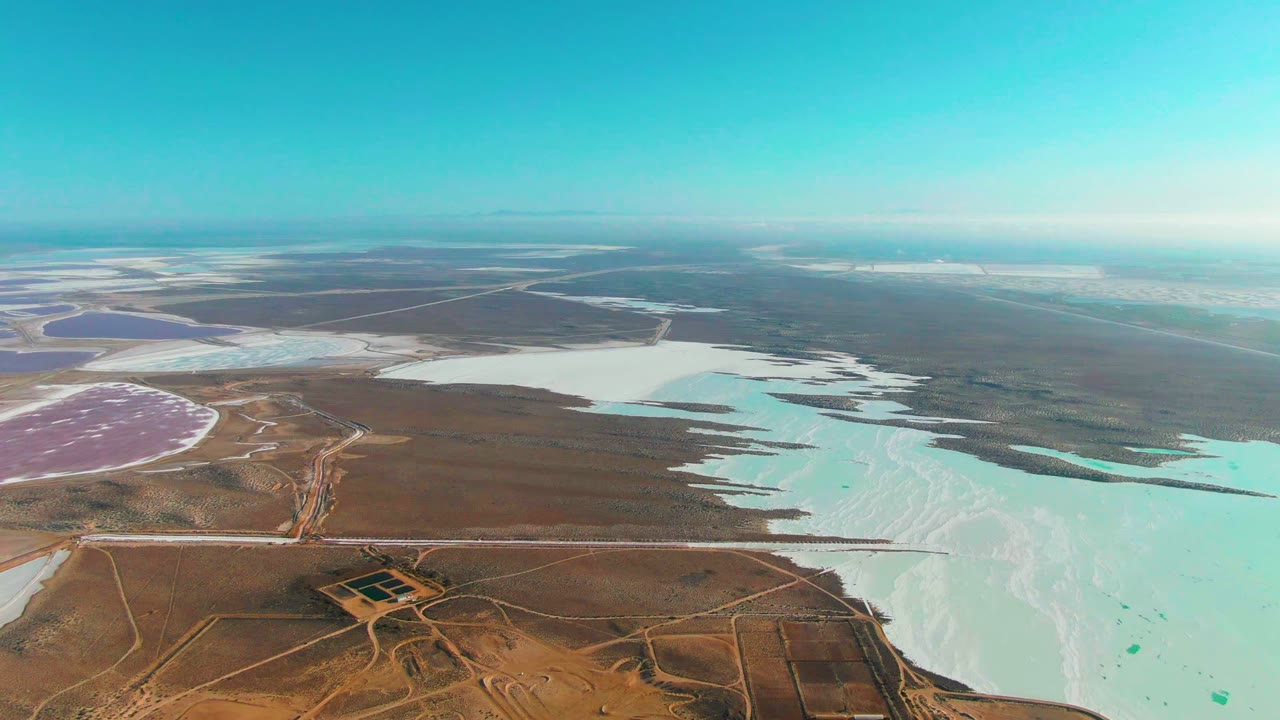 High aerial view of pale saltwater basins and desert tracks under bright sky.