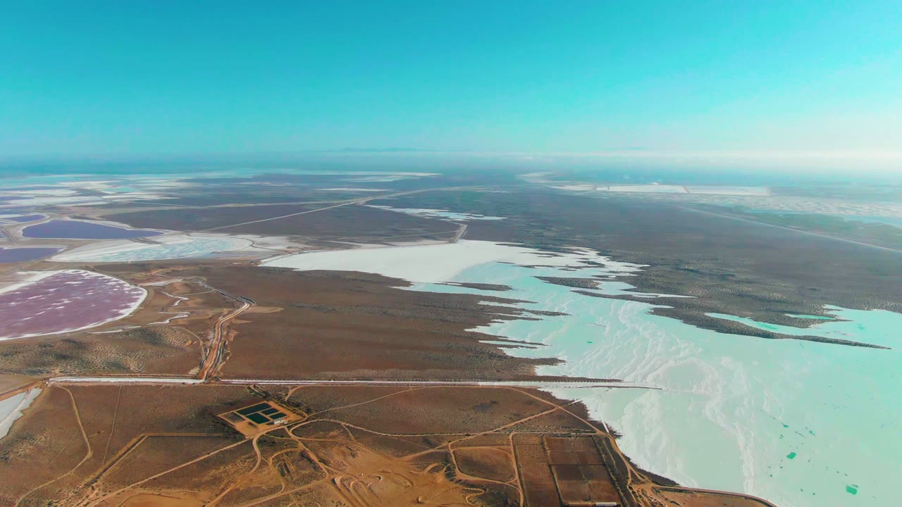 Third frame of the Guerrero Negro aerial shows turquoise and white saltwater areas meeting jagged brown shoreline edges, with distant basins and no visible people.