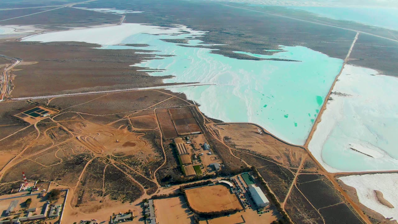 High aerial of salt evaporation ponds beside dry land and work roads.