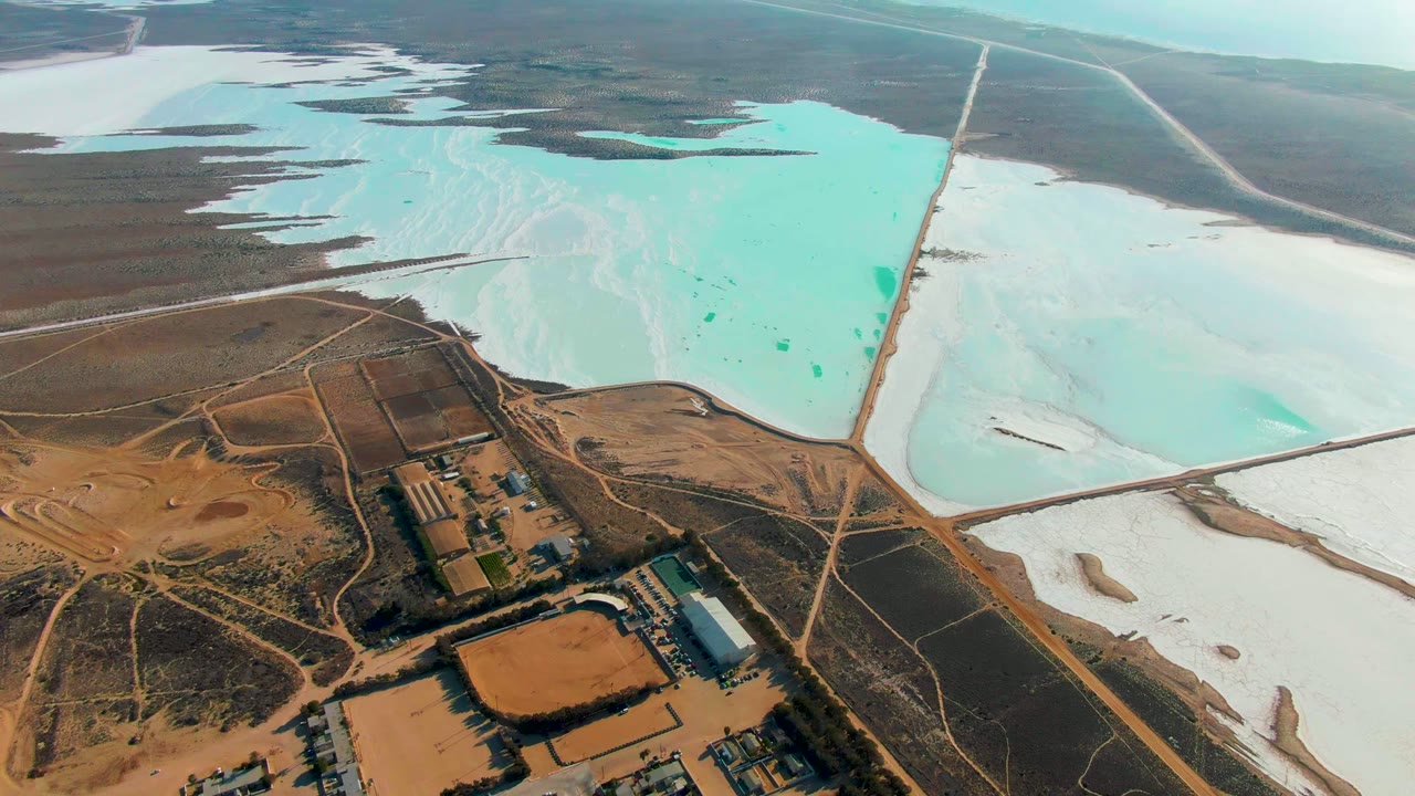 Guerrero Negro aerial view with a large turquoise evaporation pond at upper center, white deposits to the right, road embankments dividing basins, and no visible people.