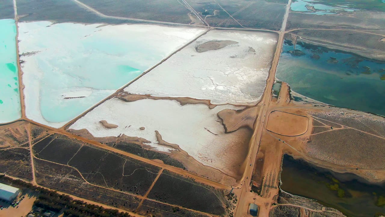 Salt flats and blue ponds seen from above with a dirt road crossing the frame.