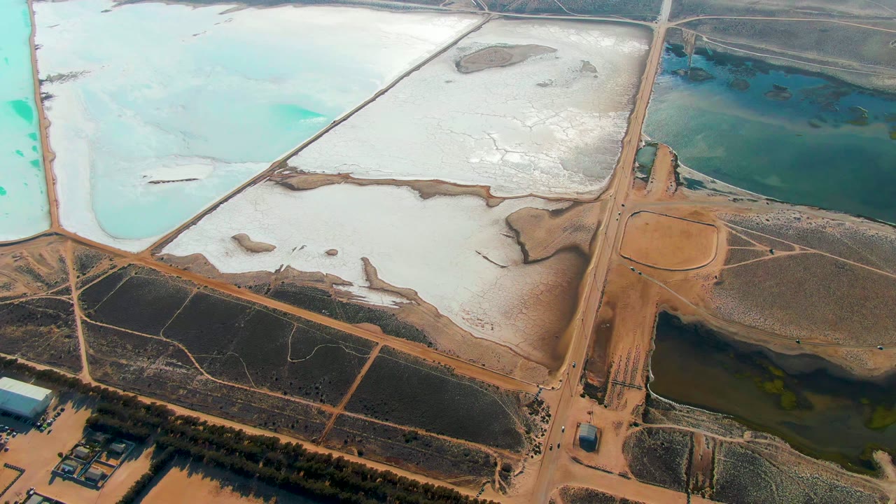 Aerial view in Guerrero Negro with a central road junction, white evaporation basin, dark water pond, turquoise pond edges, and no visible people.