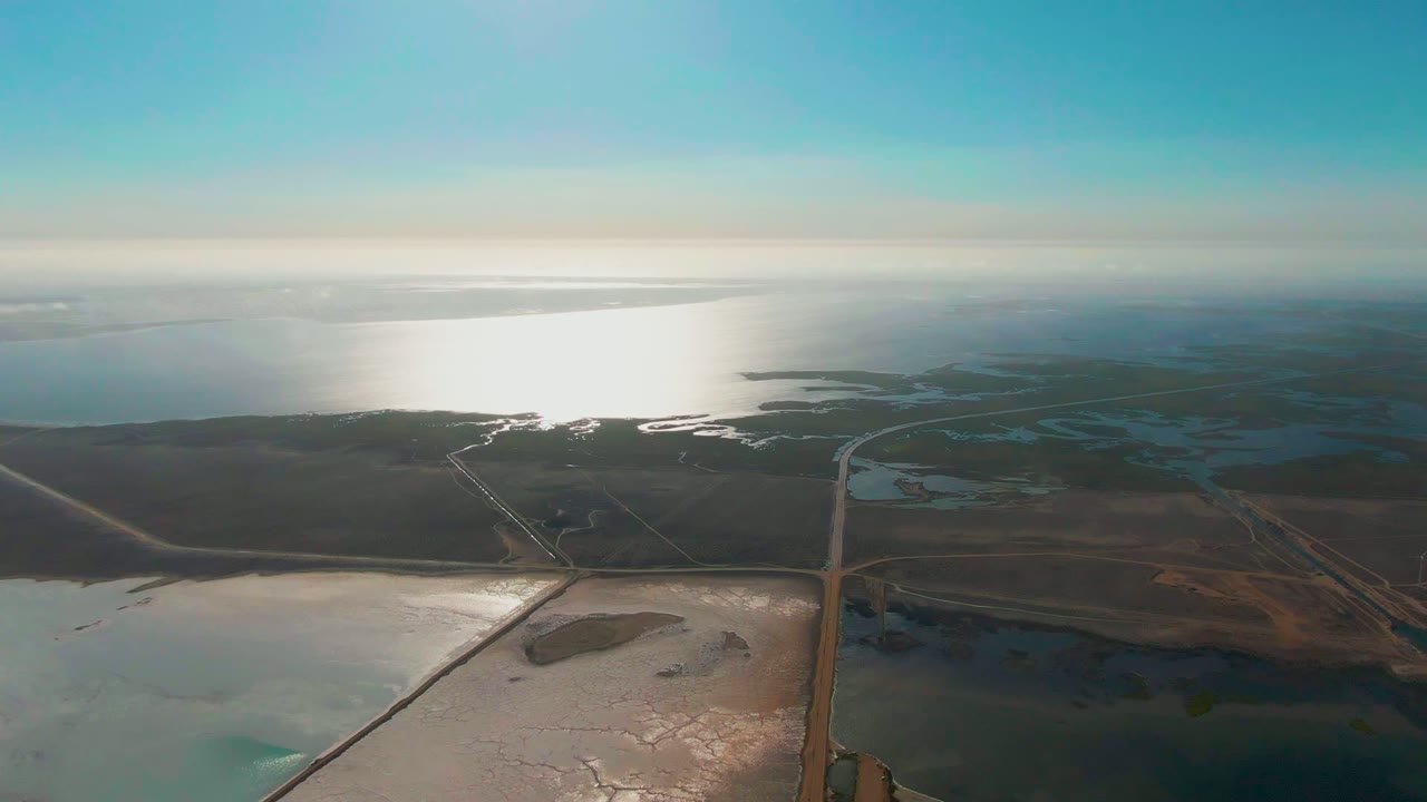 High aerial view of salt flat roads crossing shallow coastal ponds.