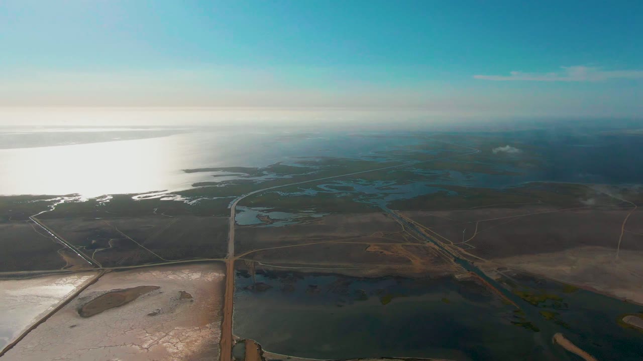 Aerial view of wetlands, fields, reflective water, and a road leading toward the horizon.