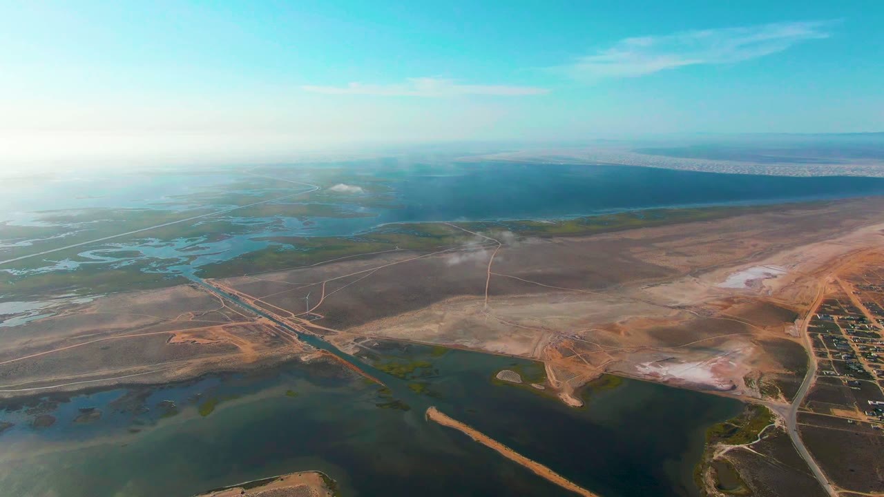 Drone-height landscape with water channels, roads, dry earth, and smoke.