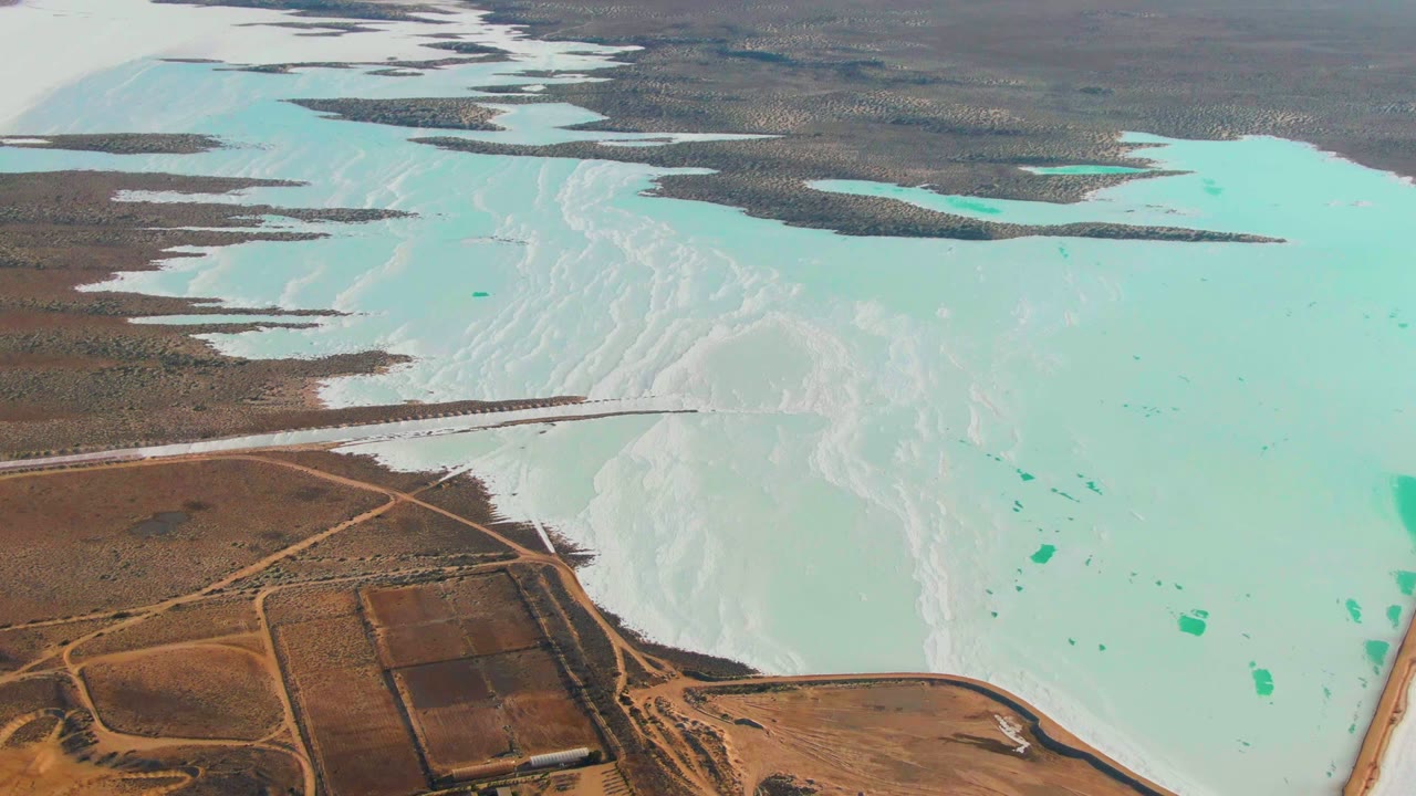 Turquoise water and white mineral deposits stretch past brown roads and rectangular ponds.