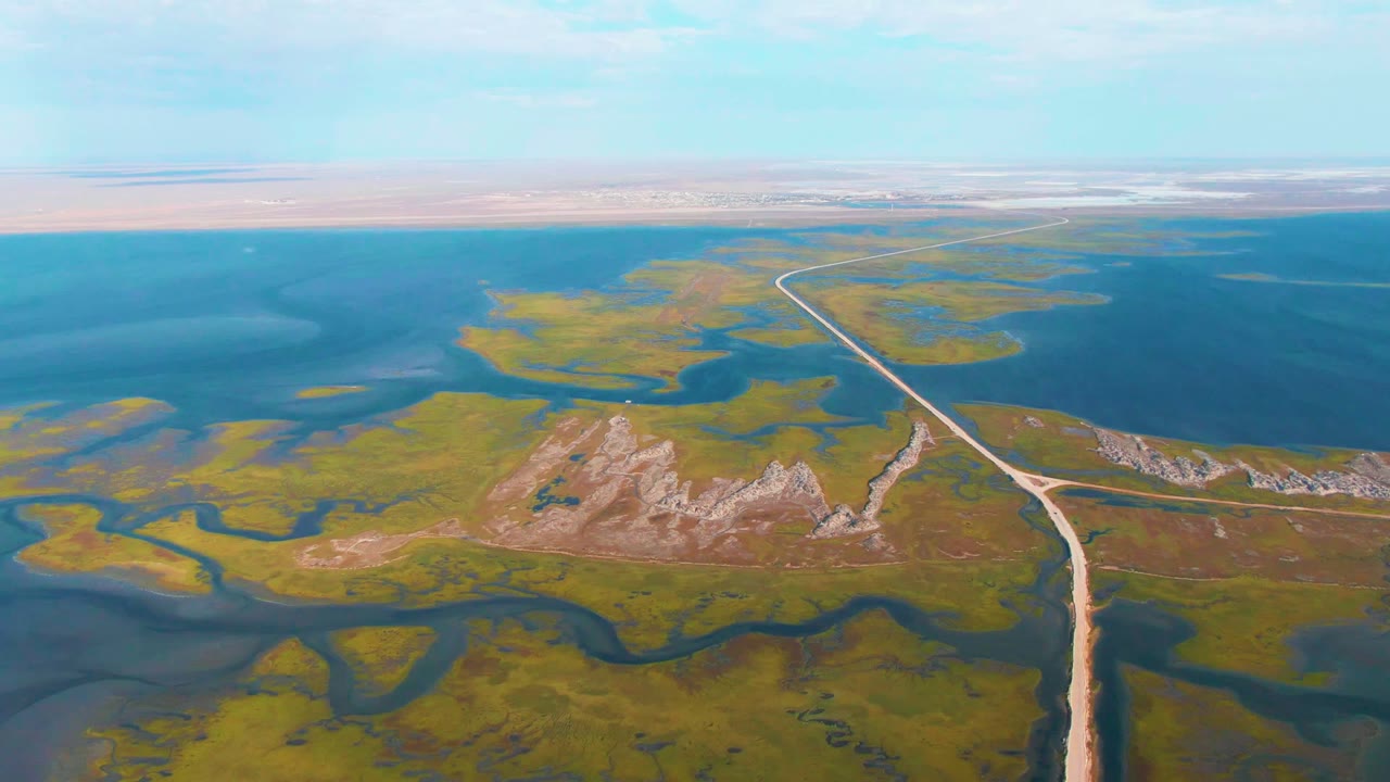 Dirt road crossing wetland channels with low rocky hills nearby
