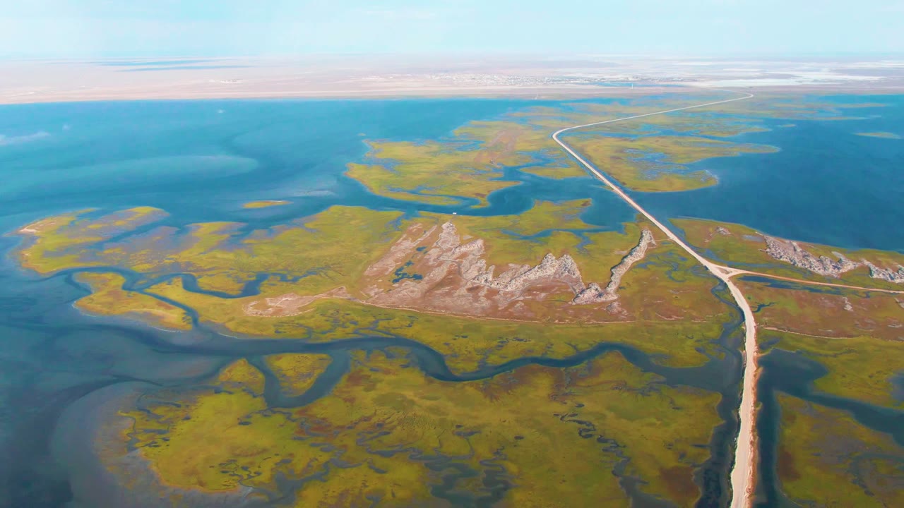 High aerial view of marsh islands, water channels, and a road with a small vehicle.