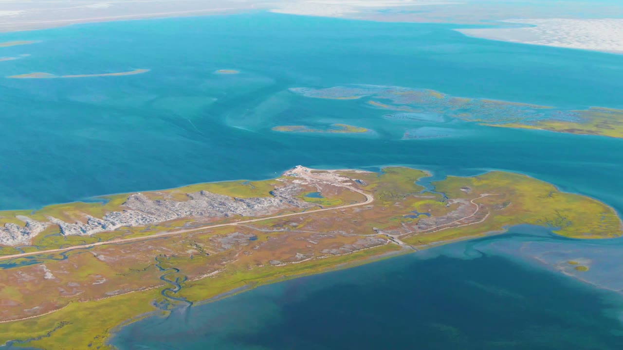 Island runway and marshy coastline seen from above blue water.