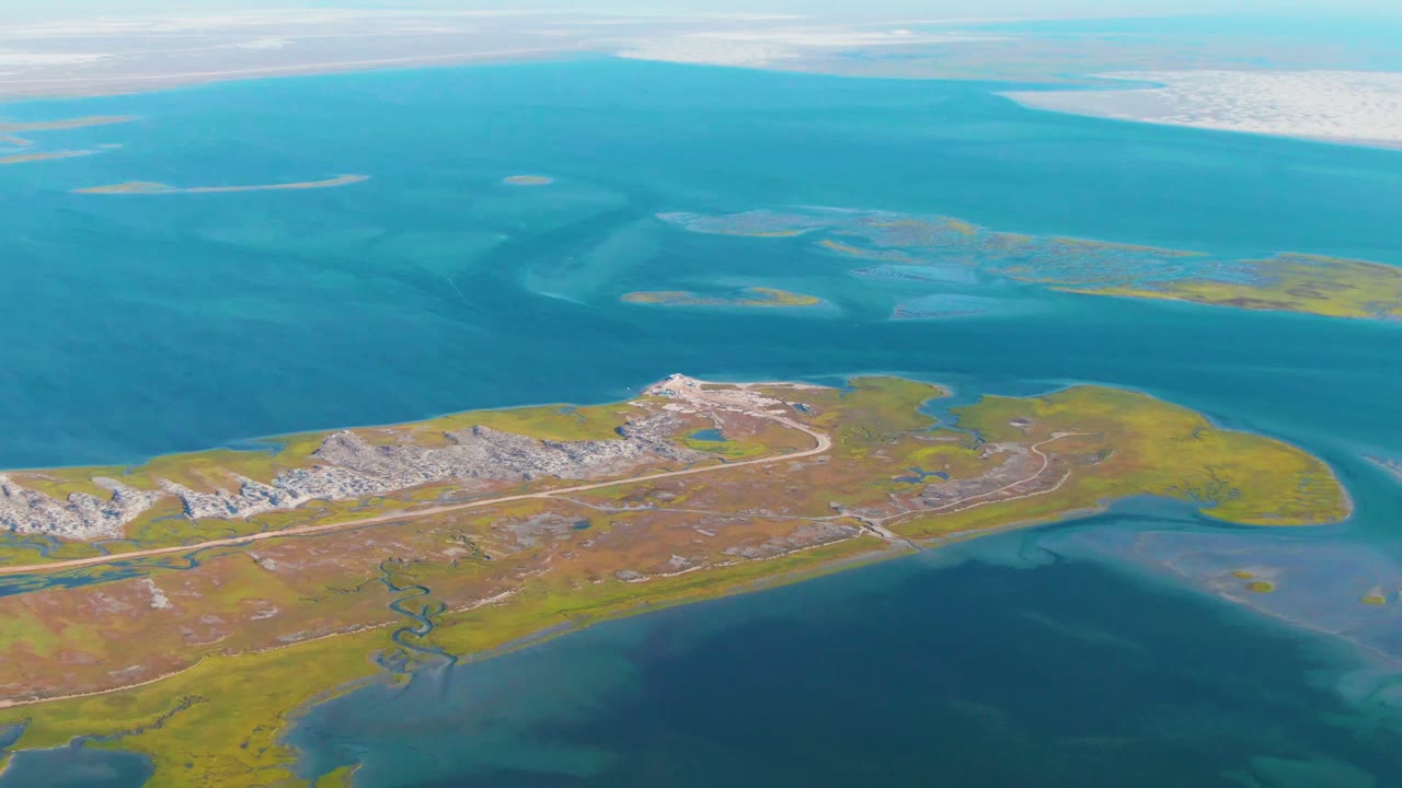 Guerrero Negro aerial frame with the island airfield stretching across the lower half, layered blue water behind it, pale white flats or shoreline in the distance, and no visible people.