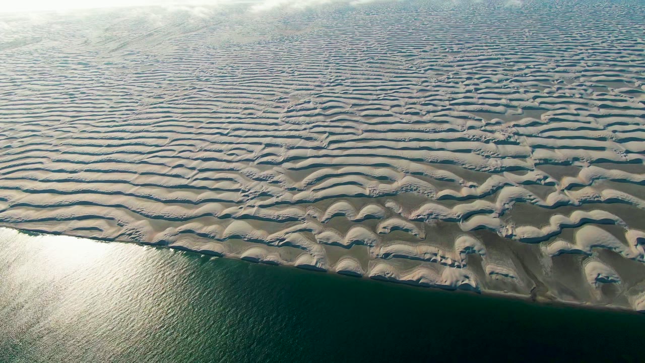 Patterned sand ridges above calm shoreline water