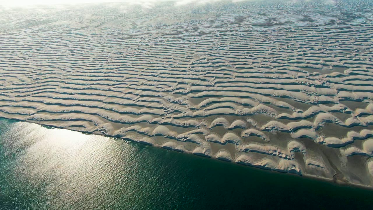 Patterned sand ridges extend toward a bright water reflection.