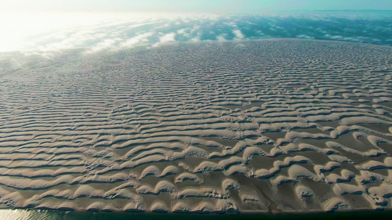 Rippled sand flats fill the frame with water along the bottom edge and clouds near the horizon.