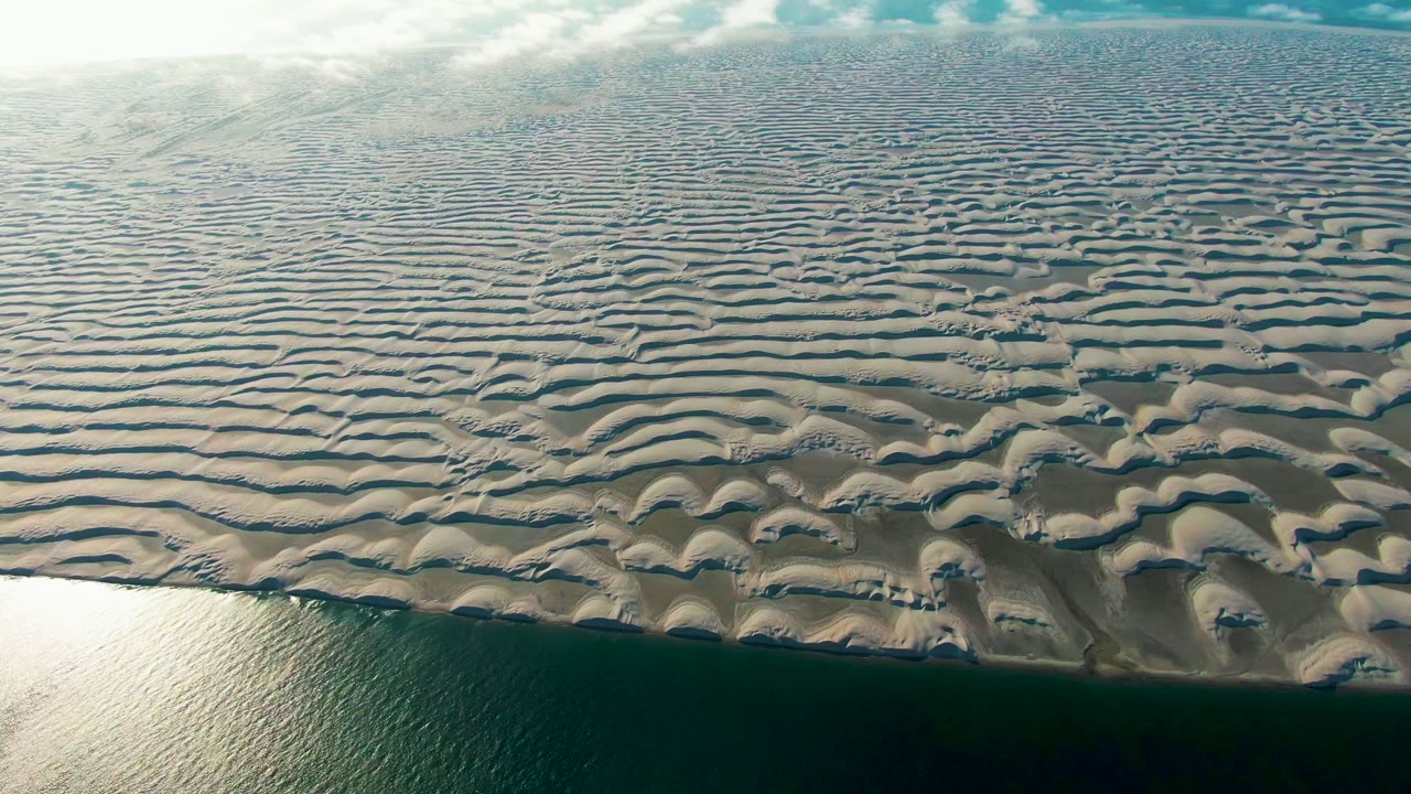High aerial view of layered sand ridges above a calm ocean edge.