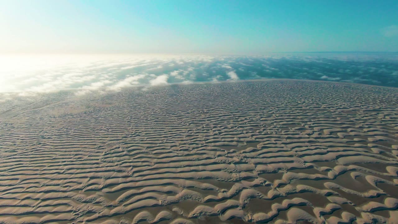 Aerial dune field with repeating sand ripples and low haze near the horizon.