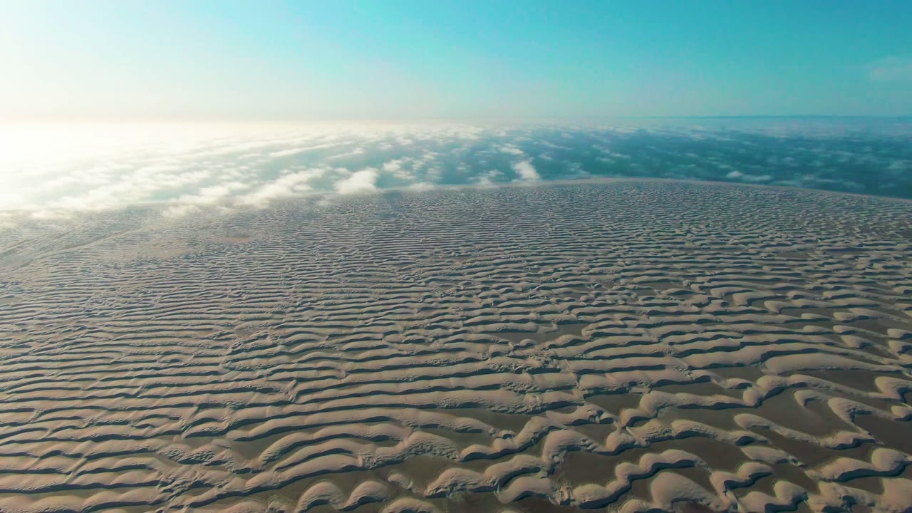At 0:02, the frame shows patterned dunes stretching toward a cloud or fog band in Guerrero Negro, Baja California Sur, with clear blue sky and no visible people.