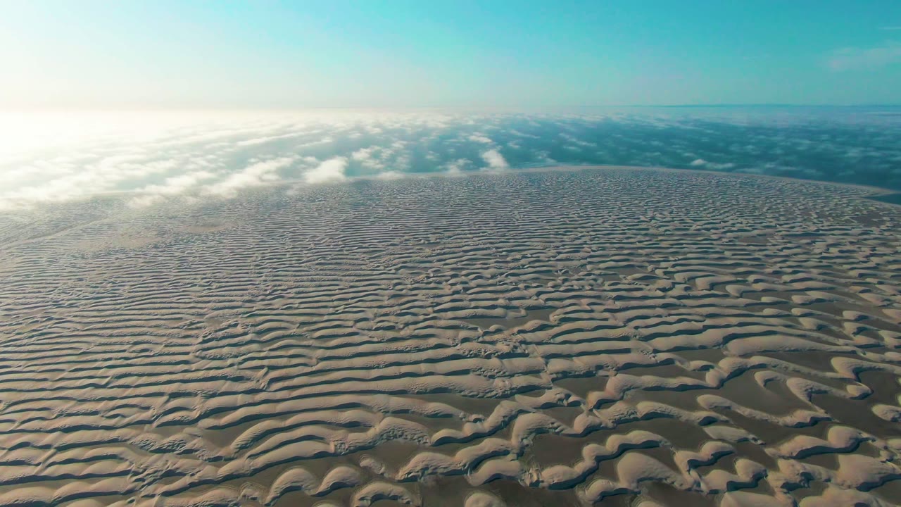 Opening frame of wind-formed sand ripples in Guerrero Negro, Baja California Sur, with bright light at left, distant clouds on the horizon, and no visible people.