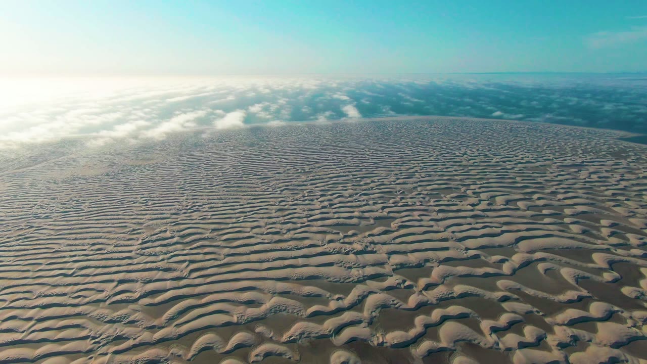 Rippled beige sand stretches toward a distant cloud band and blue sky.
