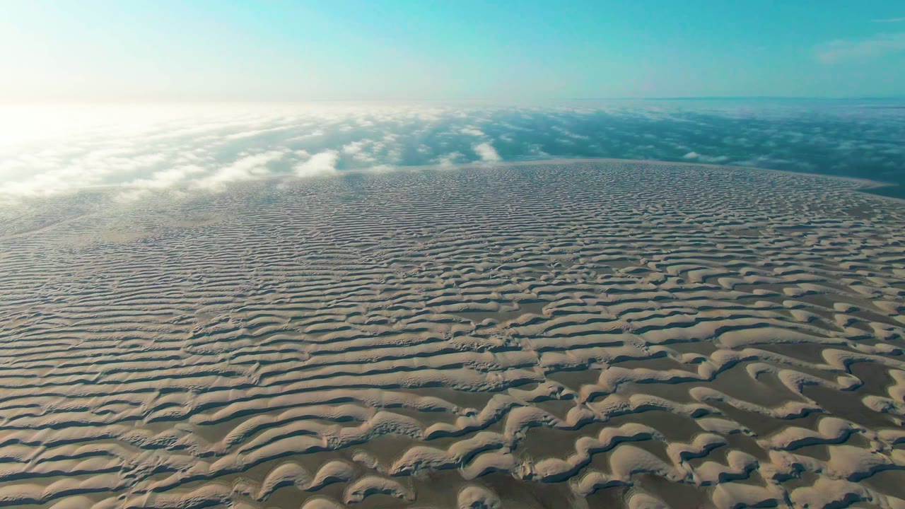 At 0:02, Guerrero Negro sand ripples remain spread across the frame, with stronger brightness on the left edge, blue sky above, and no visible people.