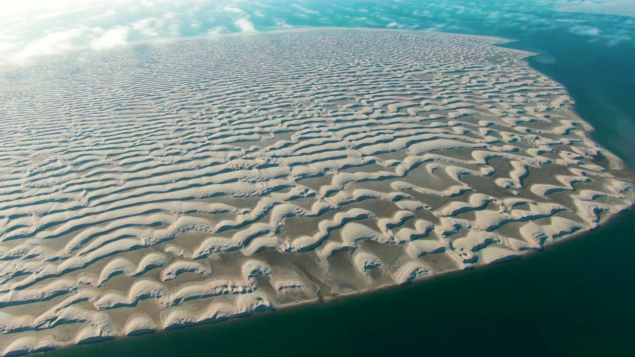 Opening aerial frame over rippled sand dunes and dark coastal water in Guerrero Negro, Baja California Sur, with no visible people.